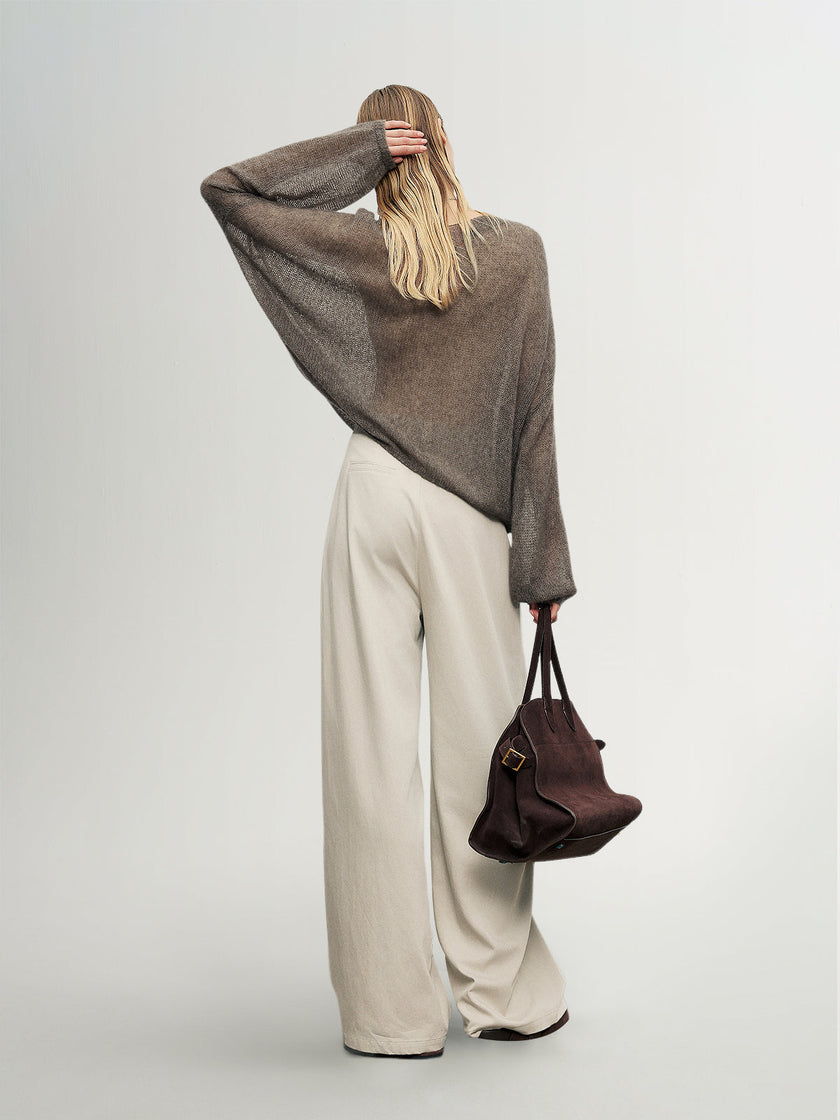Person wearing a gray sweater and beige pants, holding a brown bag on a plain background