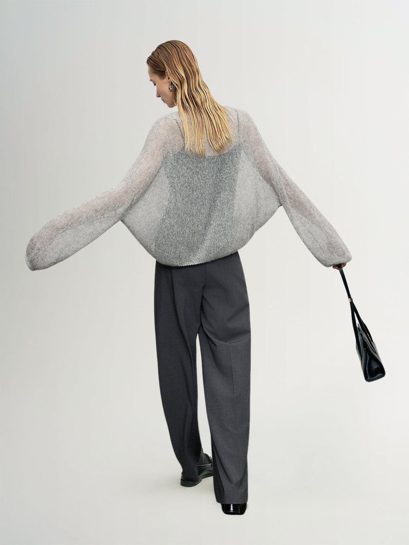 Person wearing a gray sweater and black pants holding a black handbag on a white background