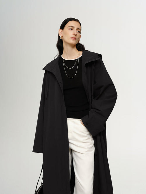 Load image 1 in gallery view. Person wearing a black coat over a black top and white pants on a plain background