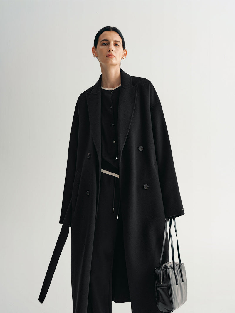 Person wearing a black midi coat holding a handbag 
