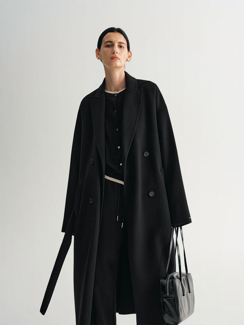 Load image 1 in gallery view. Person wearing a black midi coat holding a handbag 