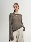 Woman wearing a brown sweater and white pants against a plain background