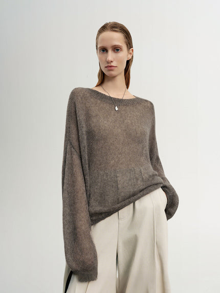 Woman wearing a brown sweater and white pants against a plain background