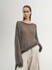 Woman wearing a brown sweater and white pants against a plain background