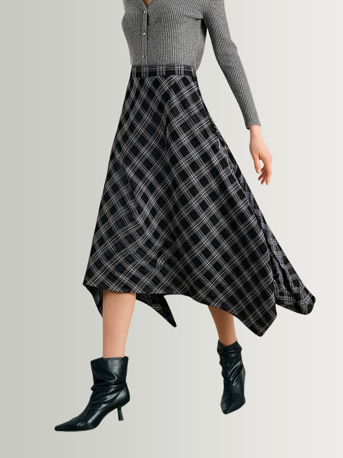 Person wearing a black and white plaid skirt with a gray top on a light gray background