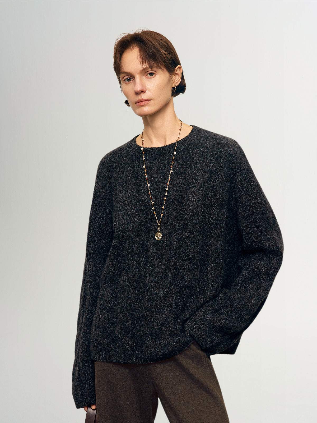 Person wearing a dark sweater and brown pants against a plain background