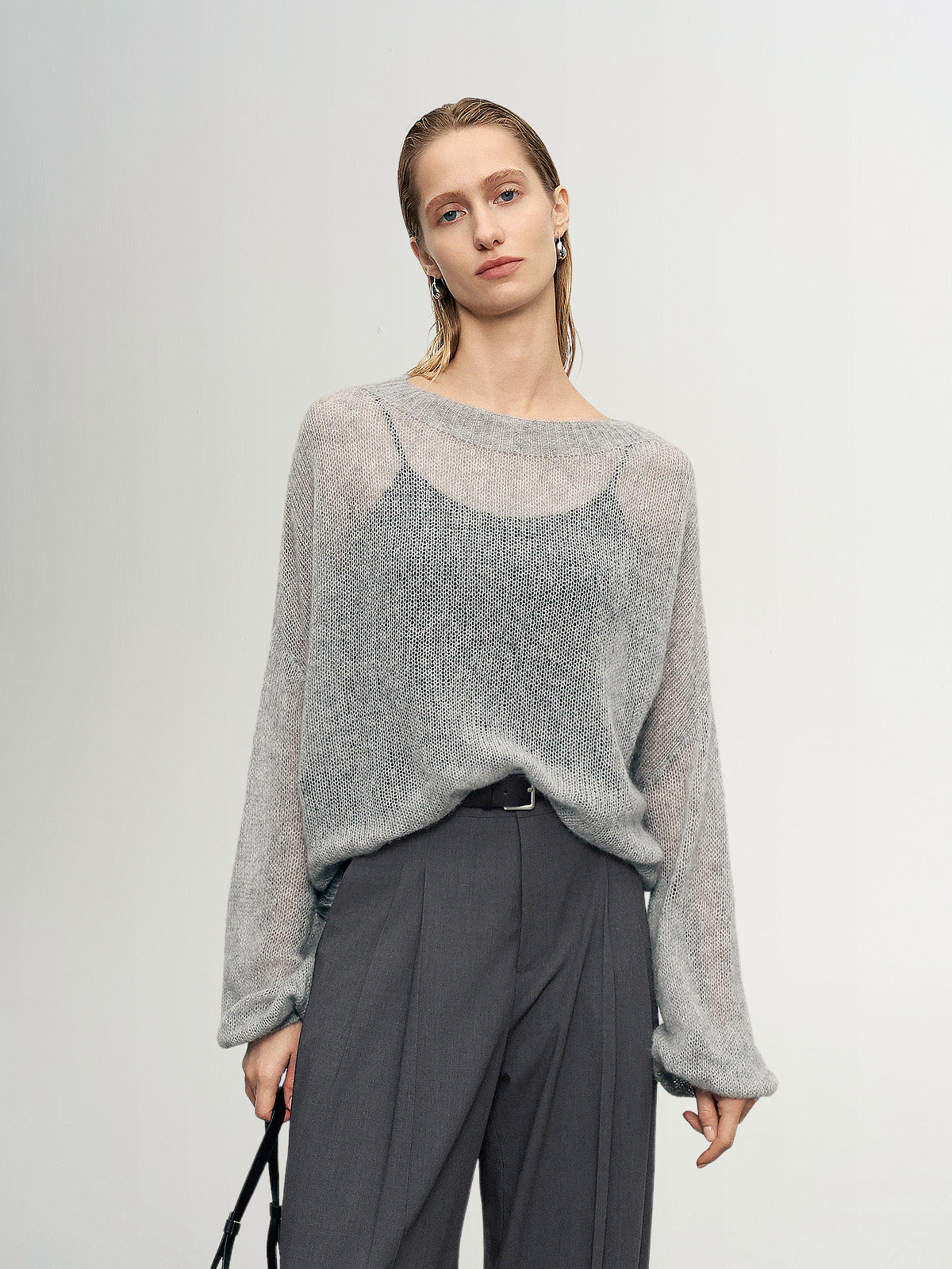 Woman wearing a gray sweater and dark pants against a plain background