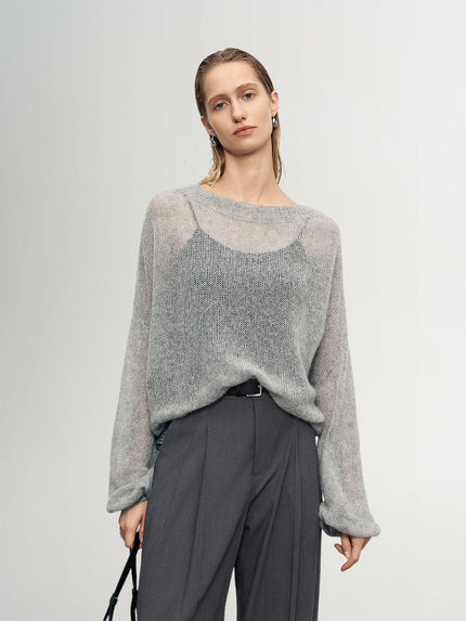 Woman wearing a gray sweater and dark pants against a plain background