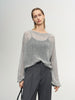 Woman wearing a gray sweater and dark pants against a plain background