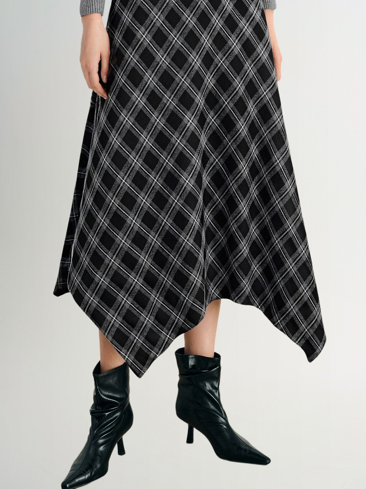 Person wearing a black and white plaid skirt with black boots on a light gray background