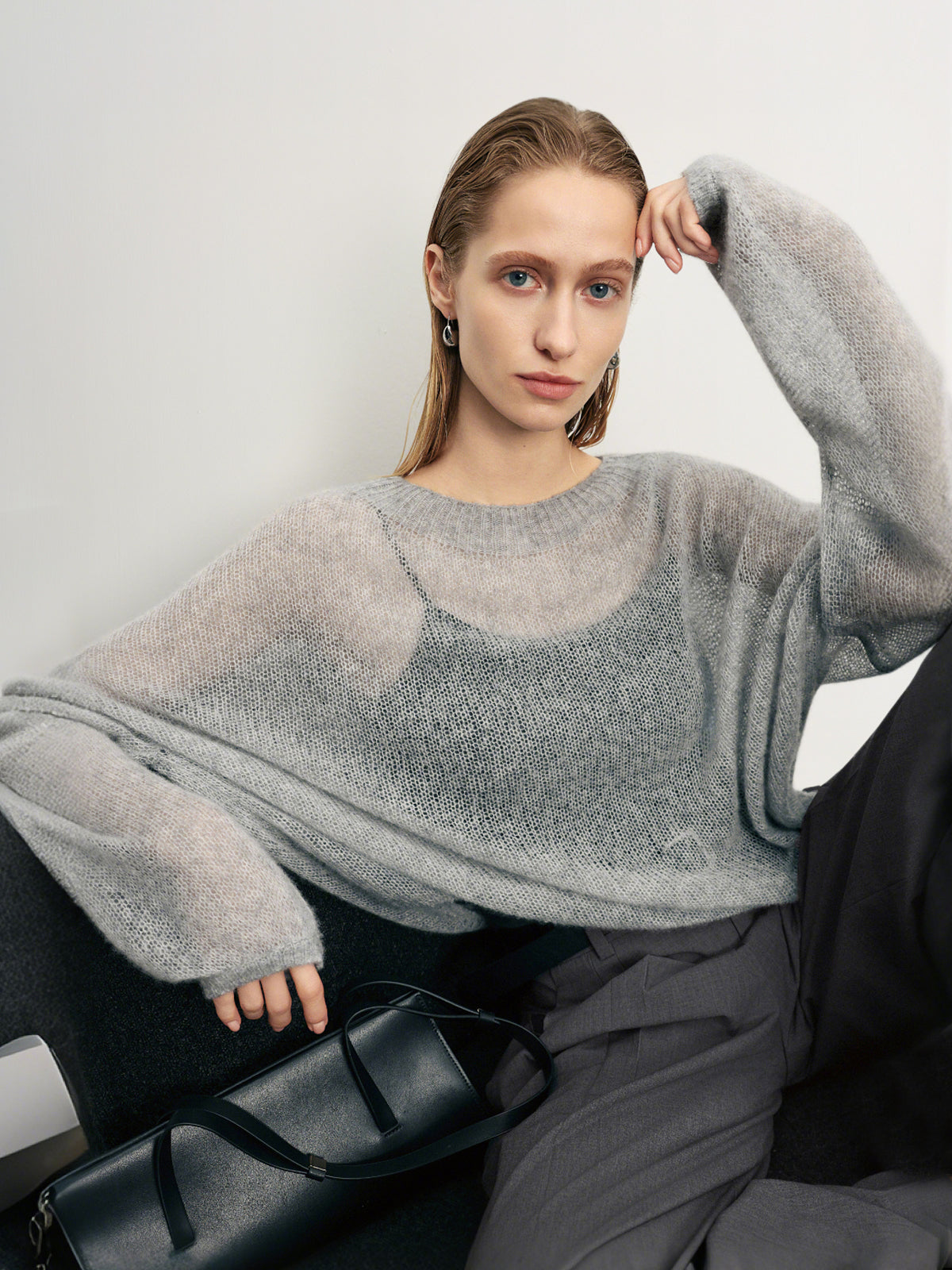 Woman wearing a gray sweater sitting on a black chair against a white background
