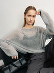 Woman wearing a gray sweater sitting on a black chair against a white background