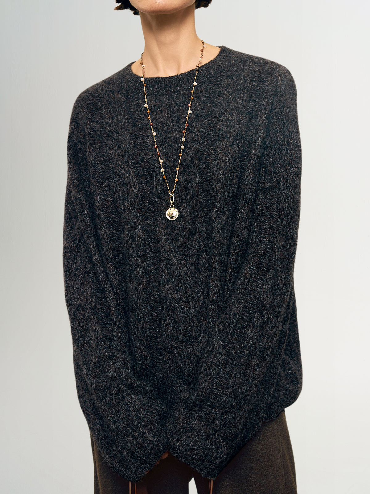 Person wearing a dark gray sweater and a long necklace with a pendant on a light gray background