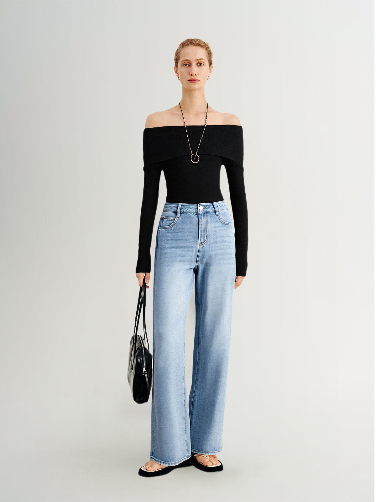 Woman wearing a black off-shoulder top and light blue jeans on a white background