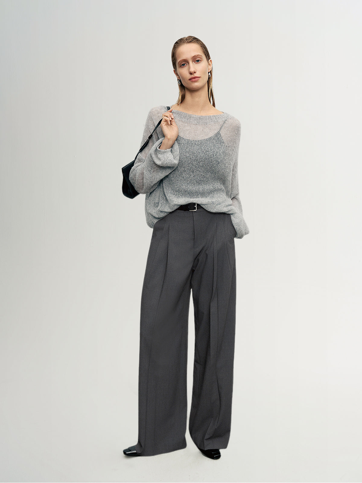 Woman wearing a gray sweater and dark gray pants against a white background
