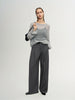 Woman wearing a gray sweater and dark gray pants against a white background
