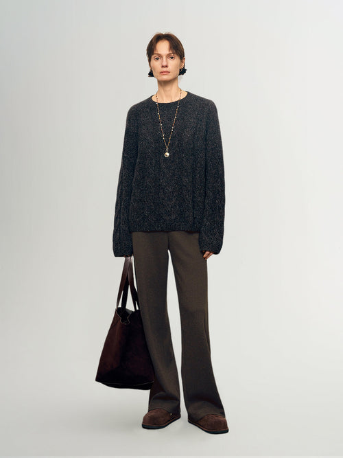 Charger l'image 1 dans la galerie. Person wearing a dark sweater and brown pants holding a bag on a light gray background