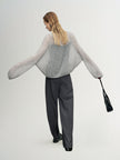 Person wearing a gray sweater and black pants holding a black handbag on a white background