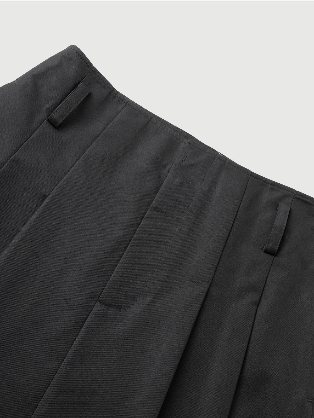 Close-up of dark gray pants with pleats on a light gray background